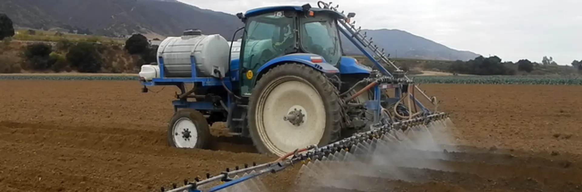 Commercial Tractor with spray boom applying pesticides to prepared vegetable beds.