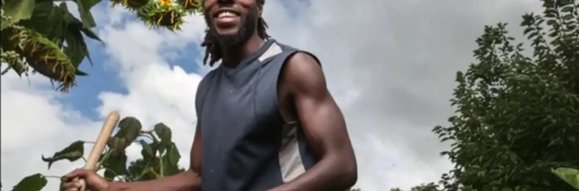 Sacramento farmer Chanowk Yisrael, shown from the waist up holding a shovel handle, stands among crops.