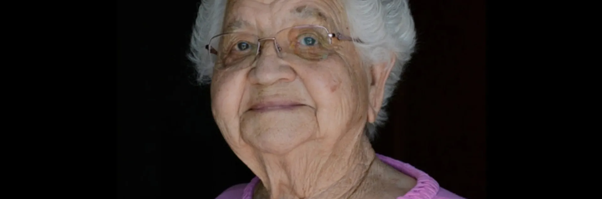 Gray haired older woman in pink top on black background