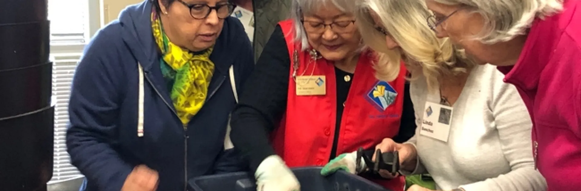 Four people gathered around an instructor with a worm composting bin to inspect the contents.