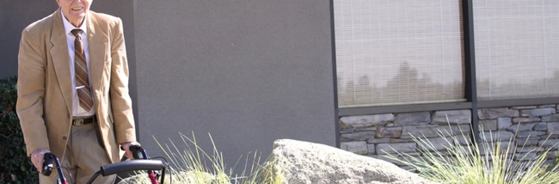 John Pehrson, standing with a walker, poses beside the building sign bearing his name.