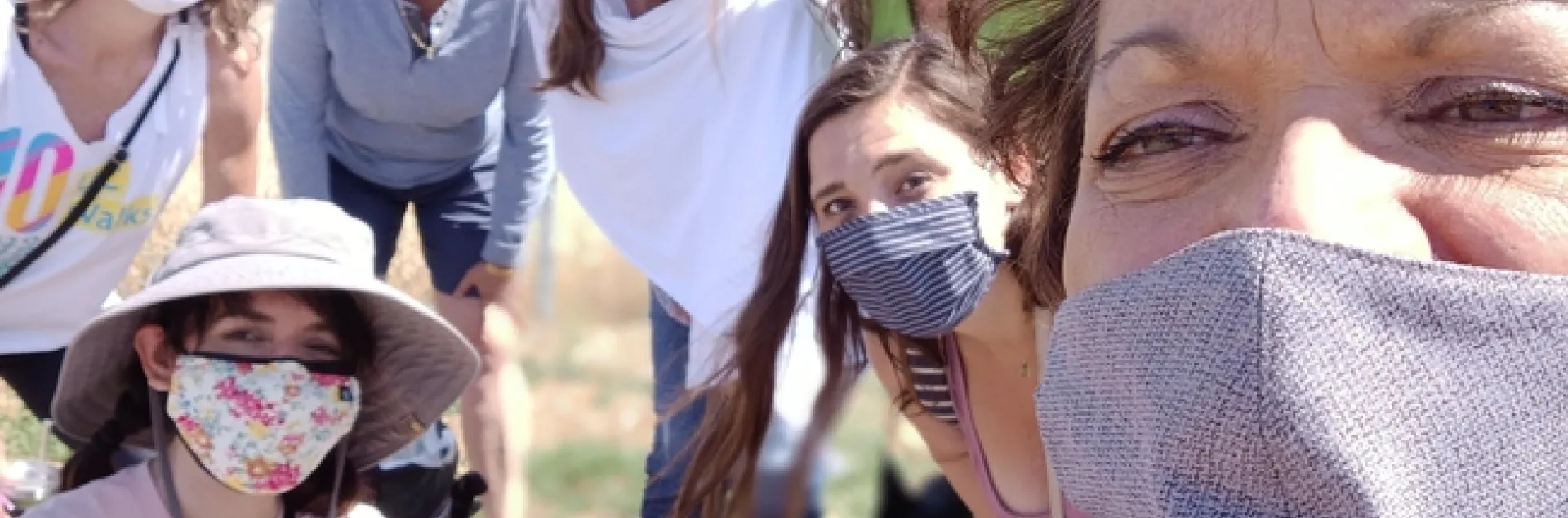 Seven people wearing facemasks and sportswear gather for a selfie outdoors.
