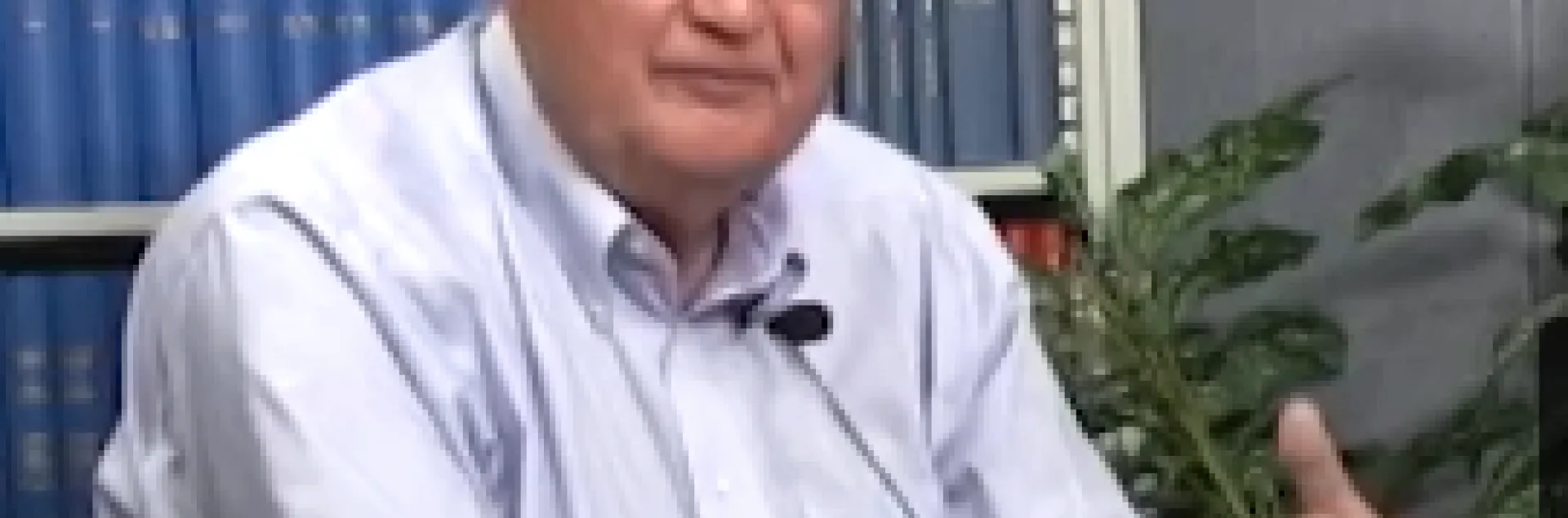 Jim Clawson sitting in front of a bookcase and a potted plant.