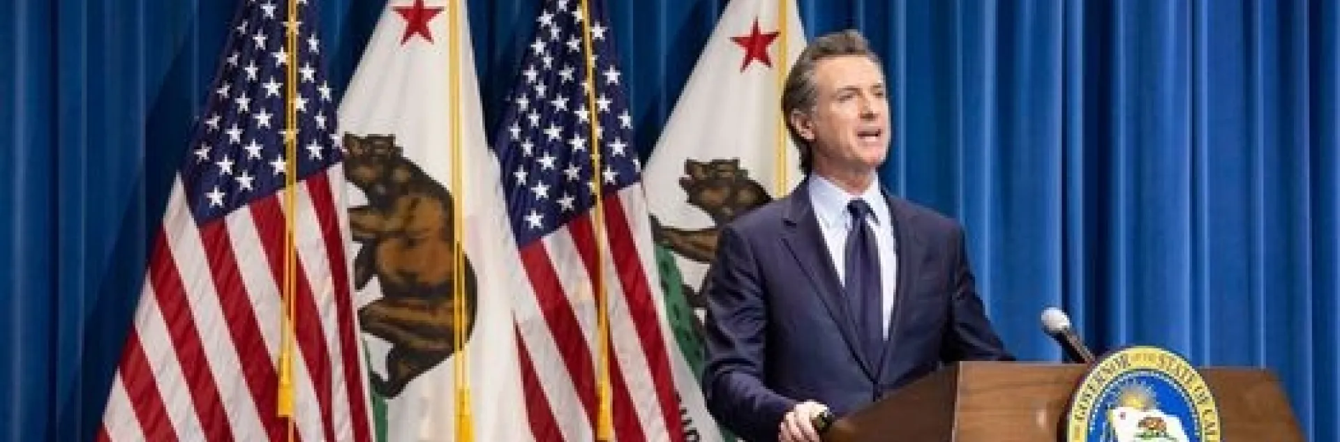 The governor stands at a lectern in front of four flags -- 2 US flags and 2 California flags alternating.