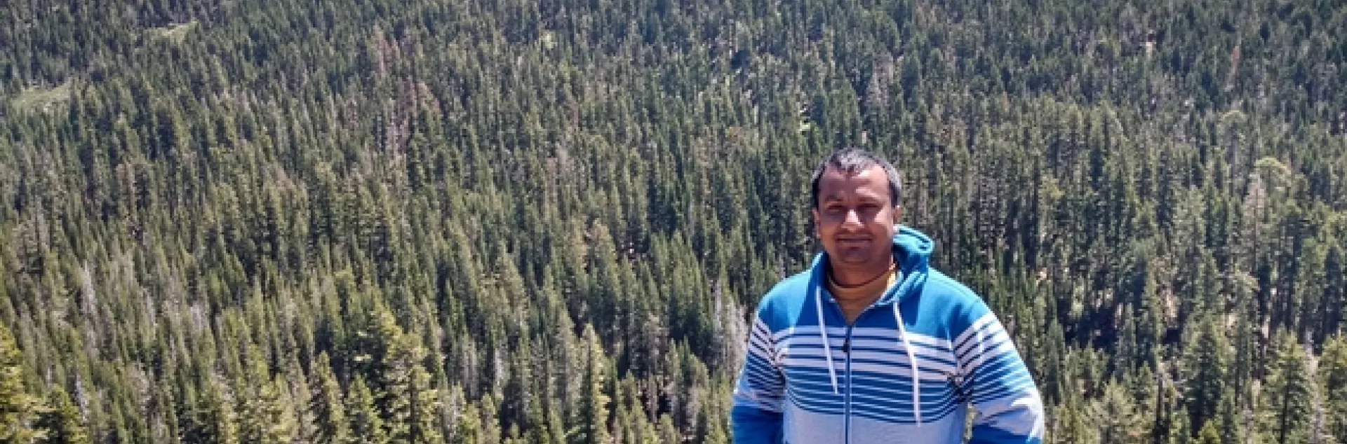 Khan smiles from a cliff with acres of forest stretch out behind him.