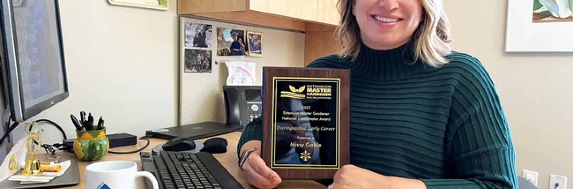 Missy at in her office holding up her award plaque.
