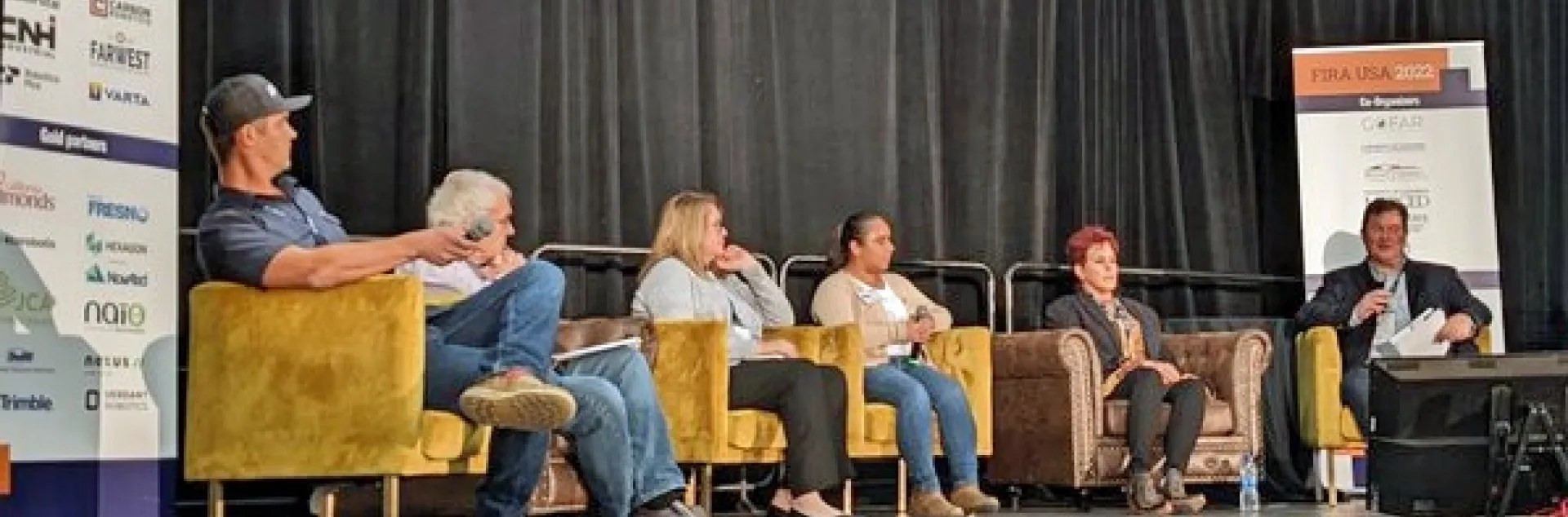 Panelists sit in armchairs on stage.