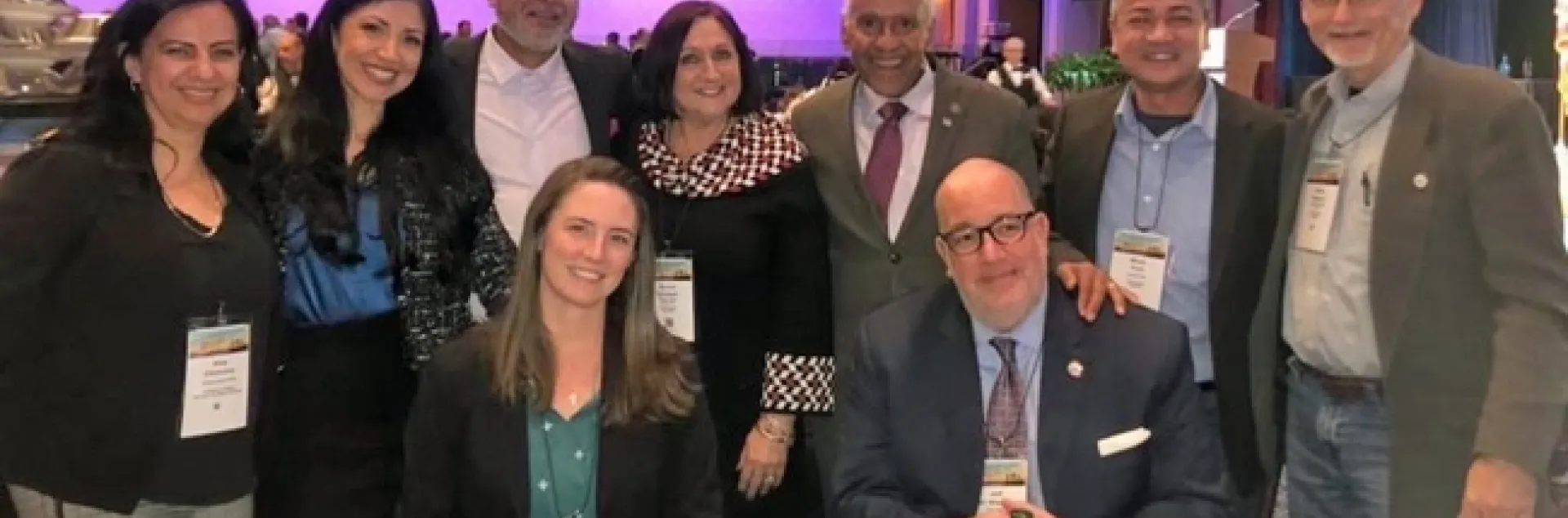 Nine people - 2 sitting and 7 standing - around a table in a conference hall.