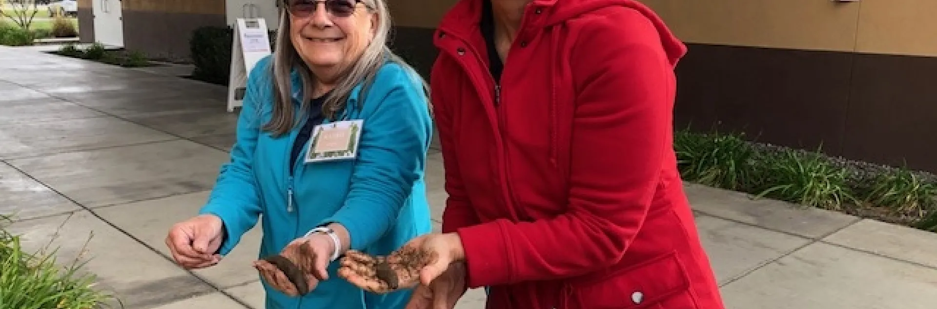 Two women holding soil samples and smiling.