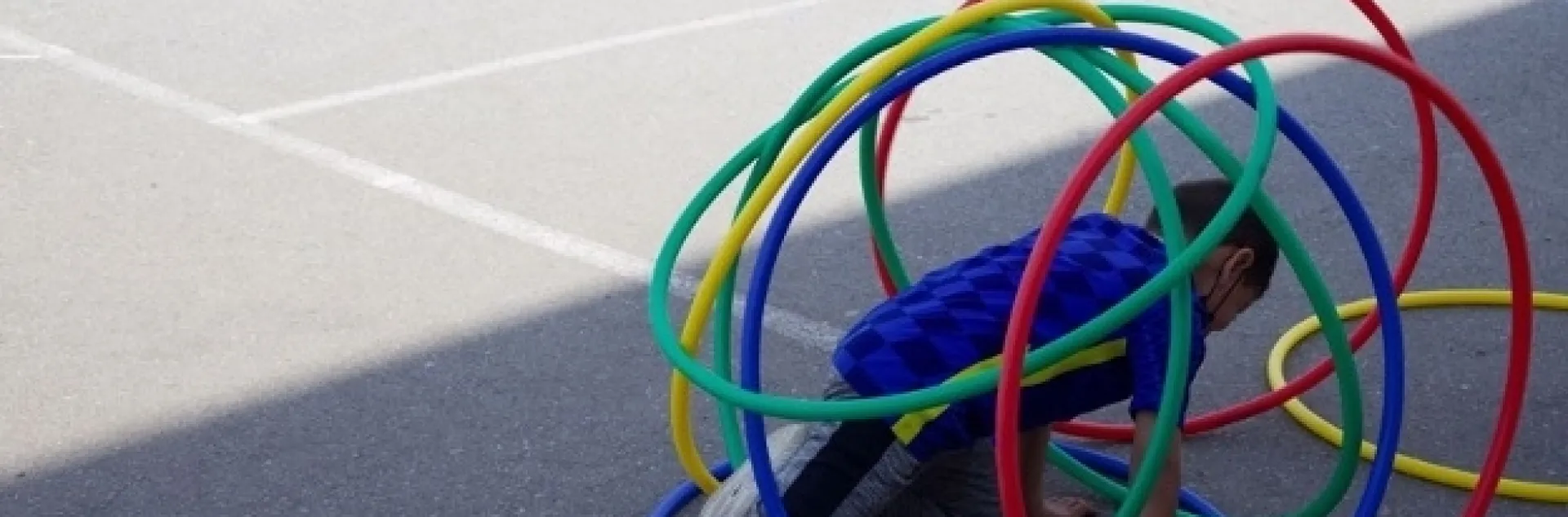 A child surrounded by red, green, blue and yellow hoops on a playground stretches his leg.