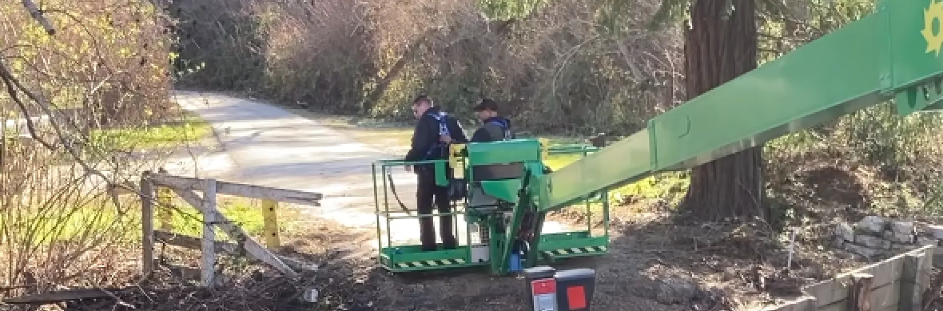 Two men stand on a green platform as the machine lowers them to the ground.