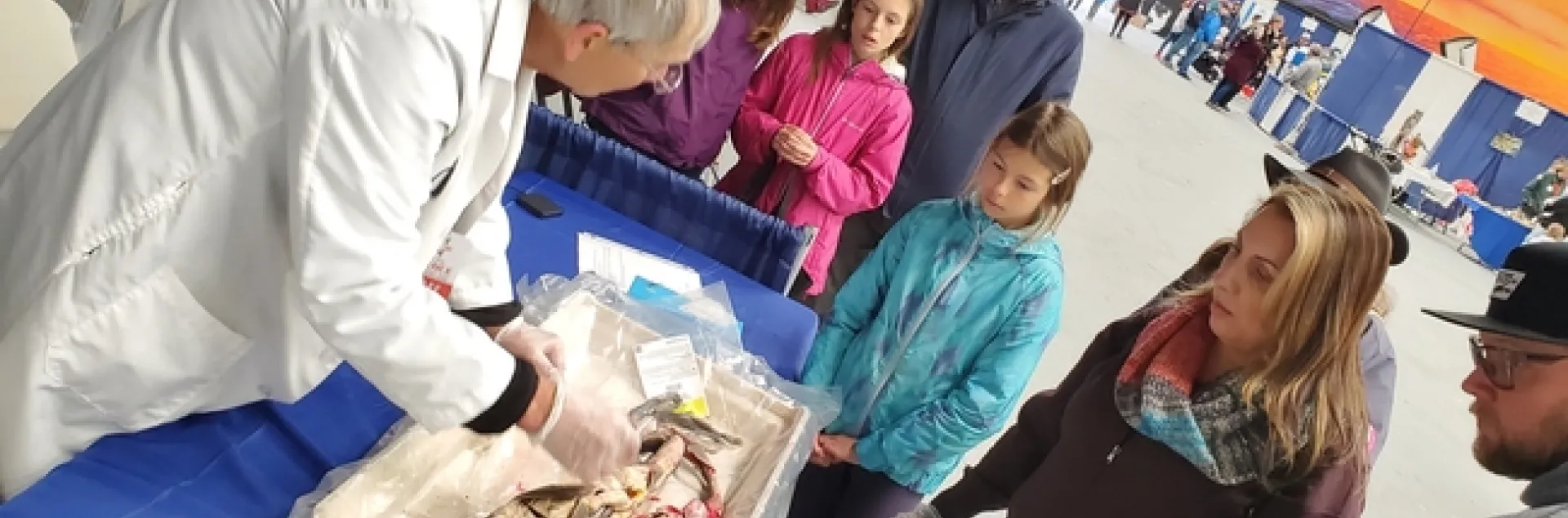 Children and parents gather around a man in a white coat gesturing to a fish that has been sliced open.