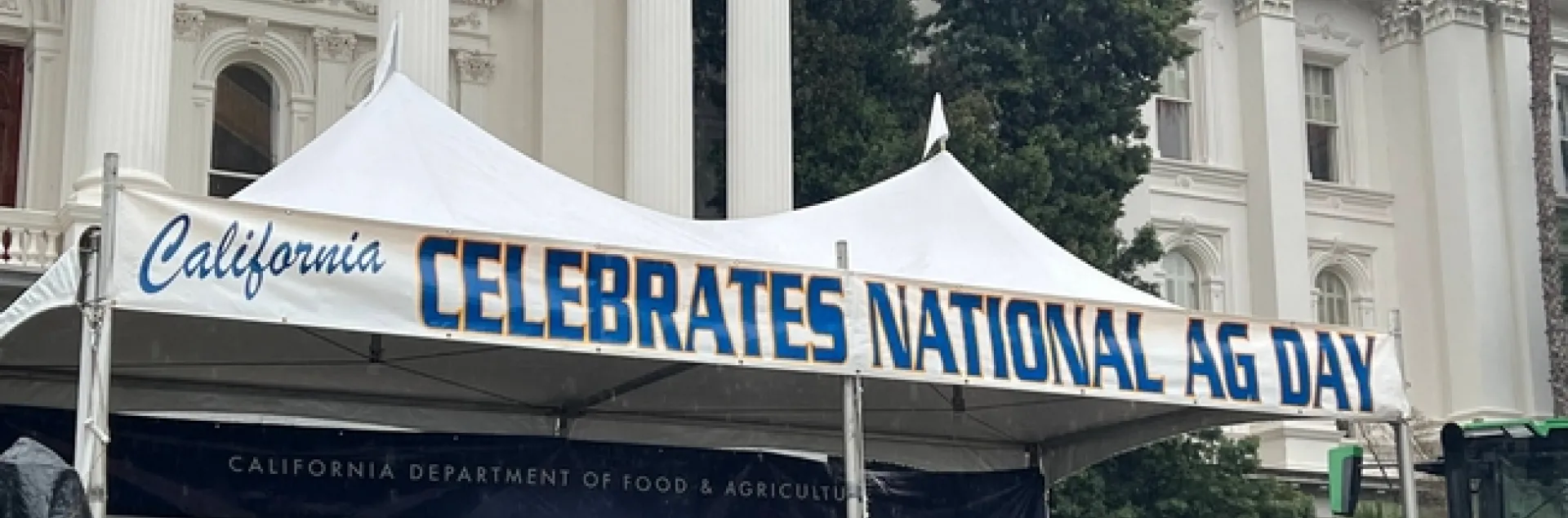 White popup canopy with the words: "CALIFORNIA CELEBRATES NATIONAL AG DAY" in front of State Capitol building.