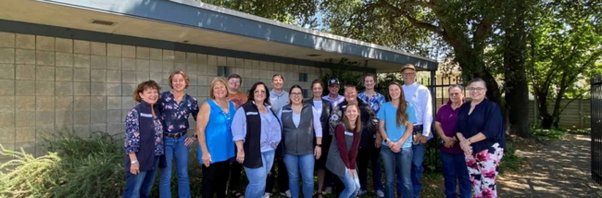 A group of people pose standing under a leafy tree.