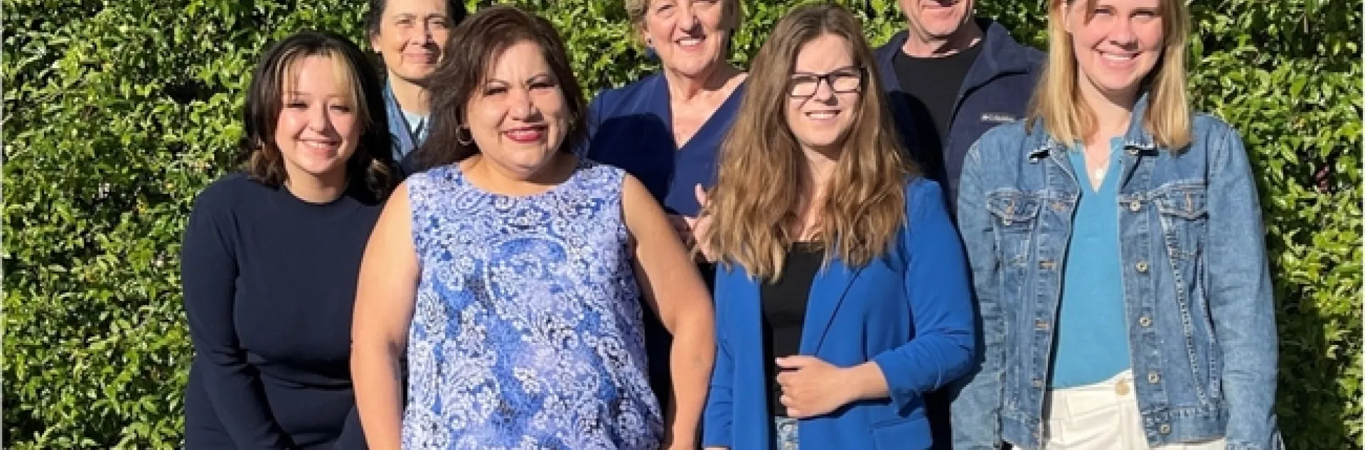 Seven people pose standing in front of flowering hedge