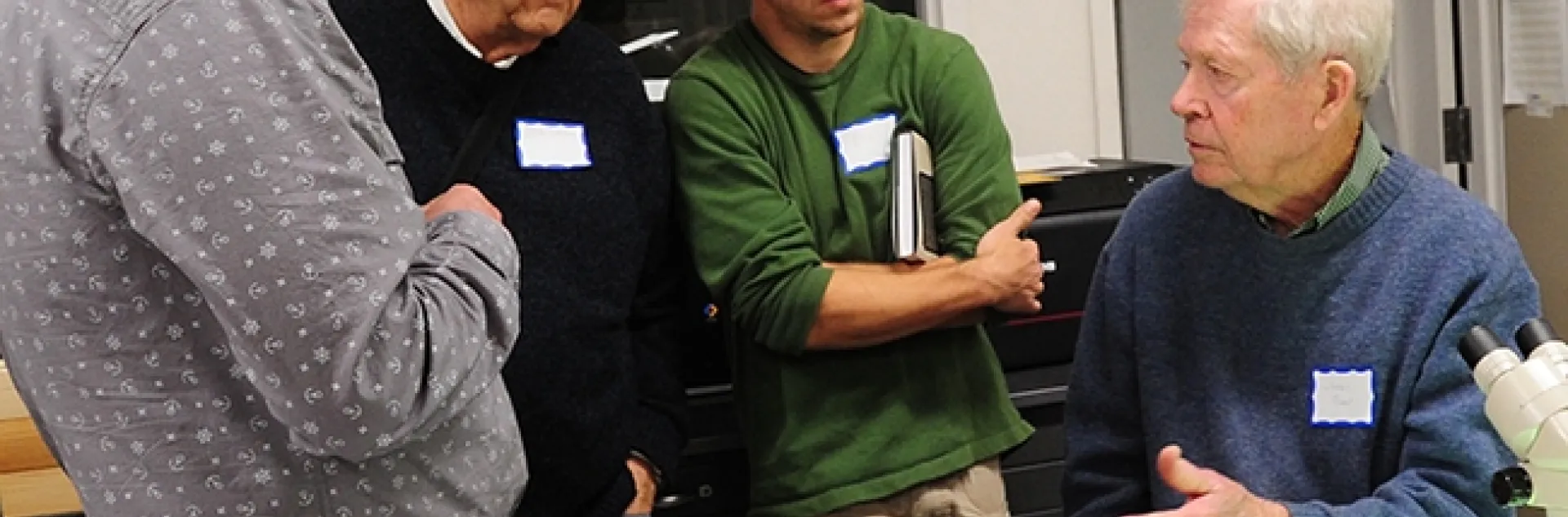 In this 2017 archived photo, Jerry Powell (seated at microscope) talks to colleagues at a Lepidopterist Society meeting at the Bohart Museum of Entomology. From left are entomologist Max Klepikov of Berkeley; UC Davis distinguished professor Don Strong of the Department of Evolution and Ecology; and Eric Lopresti, then a UC Davis graduate student. (Photo by Kathy Keatley Garvey)
