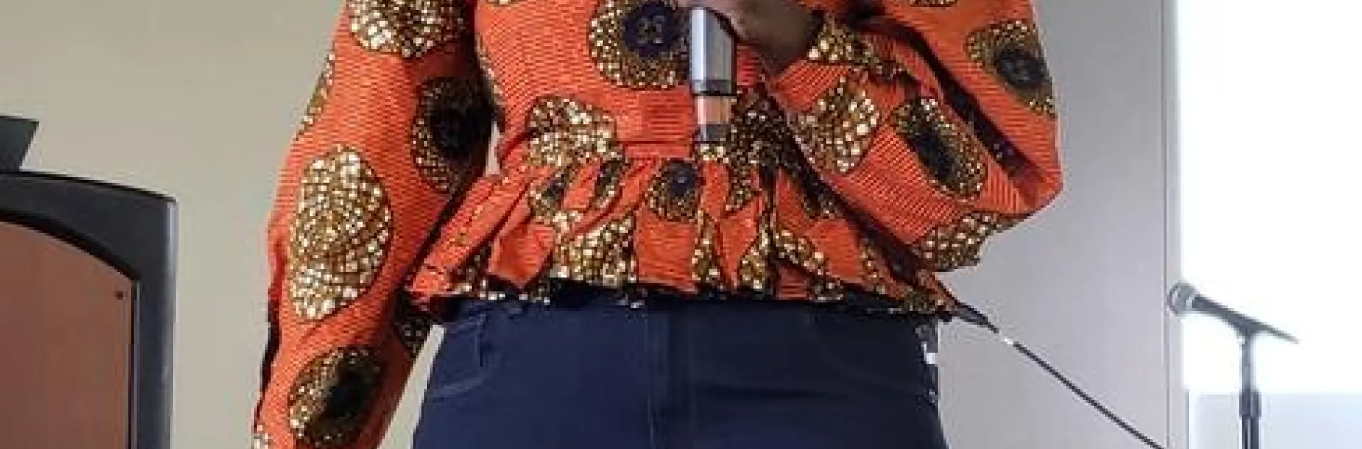 Woman wearing an orange print blouse speaks into a handheld mic.