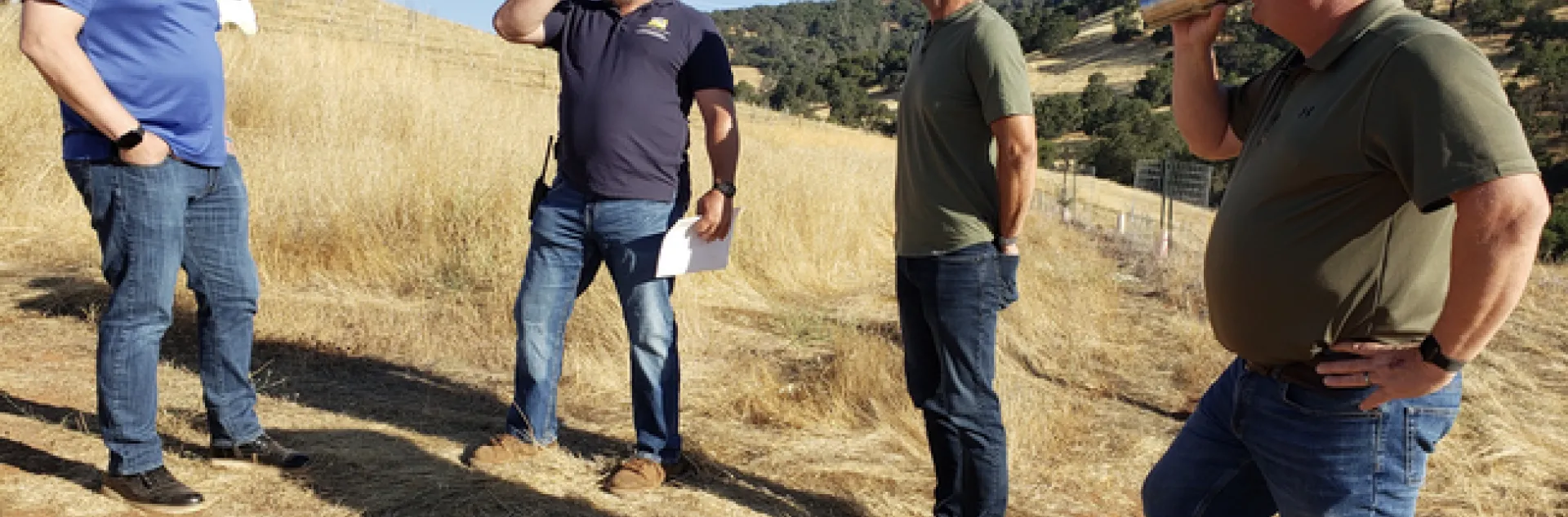 Four men stand in a dry pasture