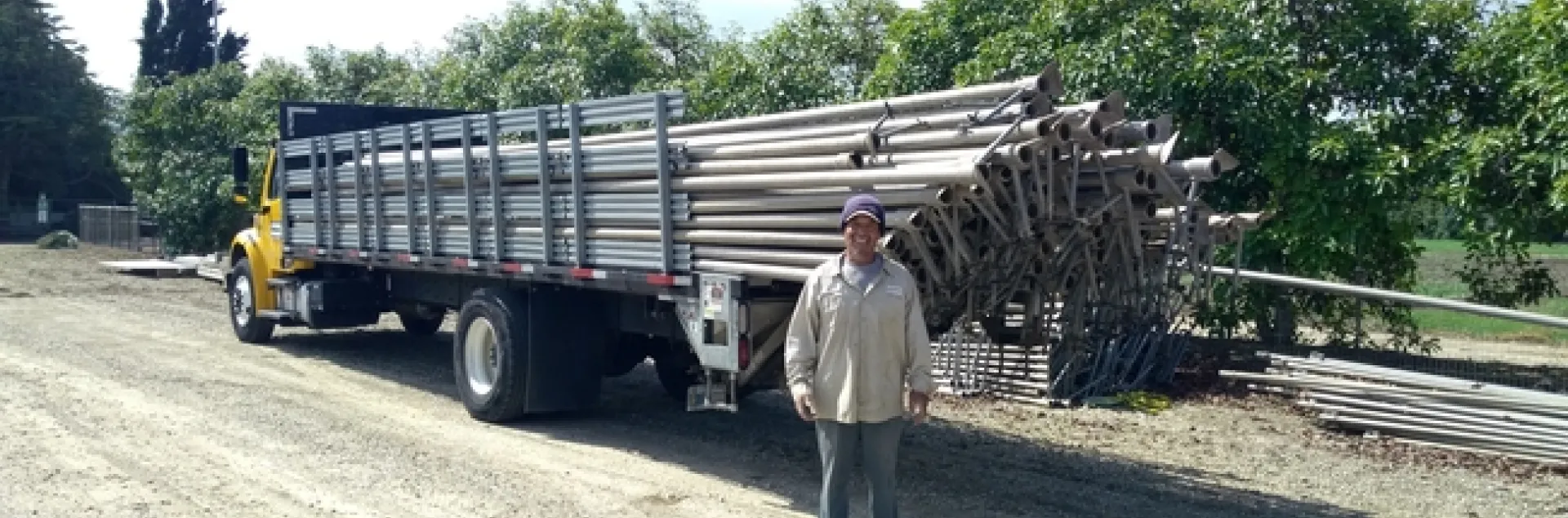 Santos stands beside a long flatbed truck loaded with irrigation pipes.