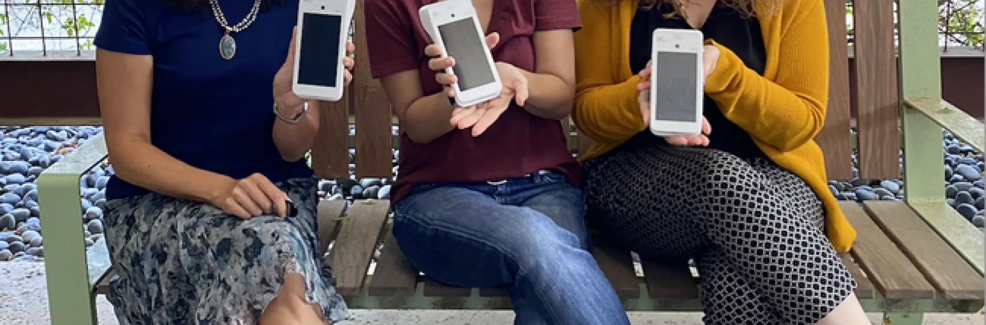 Three women sit holding credit card scanners that look like cell phones.