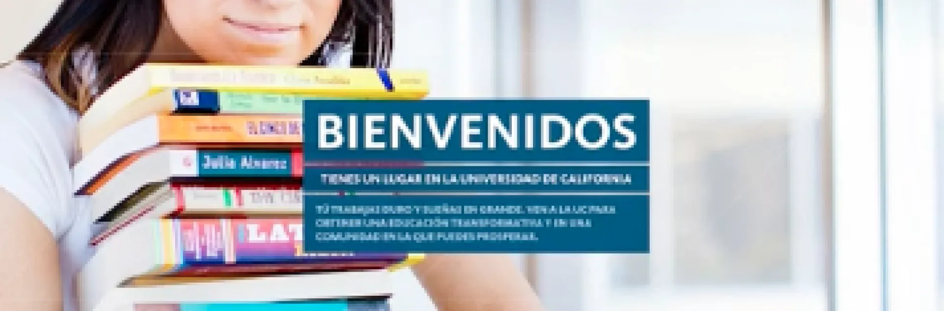 A dark-haired woman holds a stack of textbooks. Bienvenidos