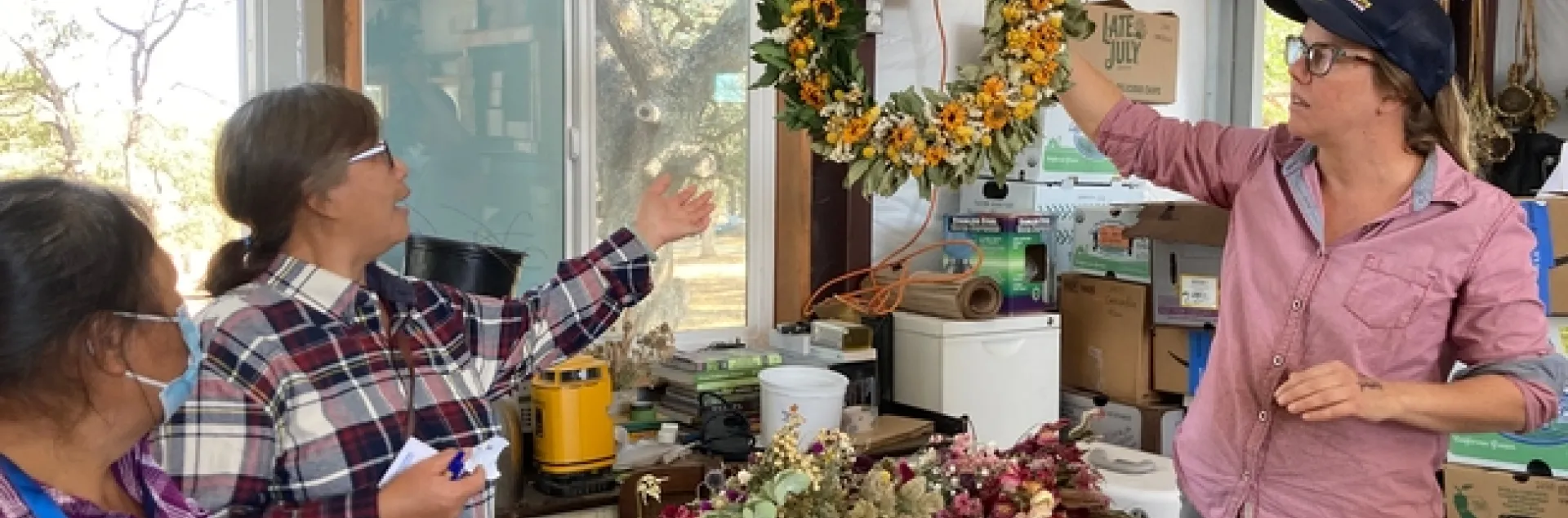 Lauren holds up a wreath made of greens and yellow flowers.