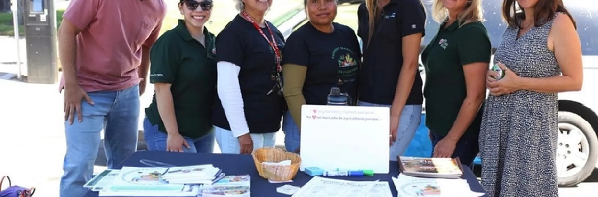 Seven people pose at a farmers market table
