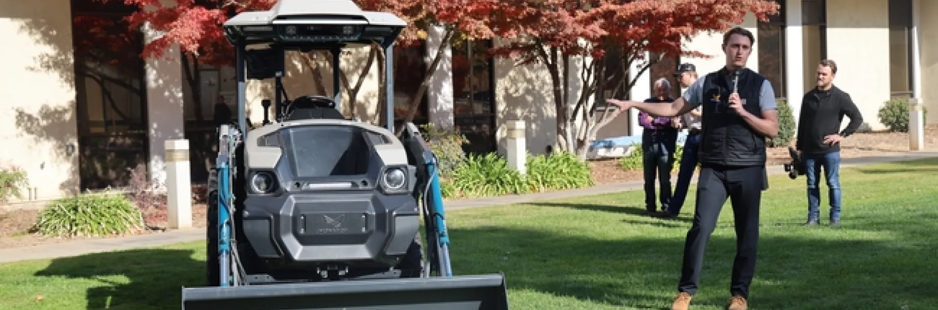 Standing on a lawn, a man gestures toward a piece of machinery.