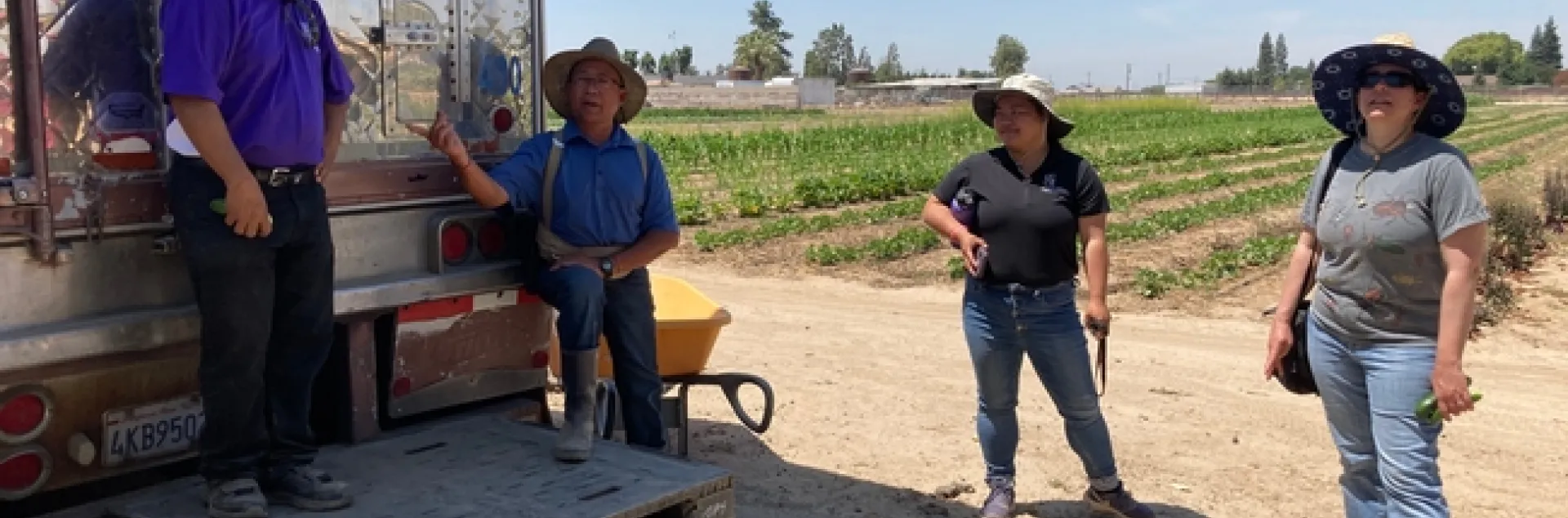 Four people stand around a refrigeration trailer next to a crop field.