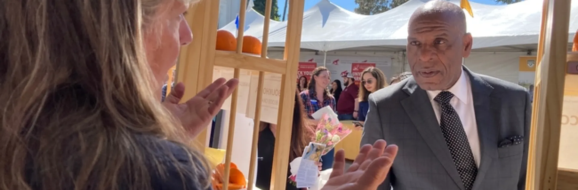 Tammy stands behind the booth table and Bradford picks up an avocado