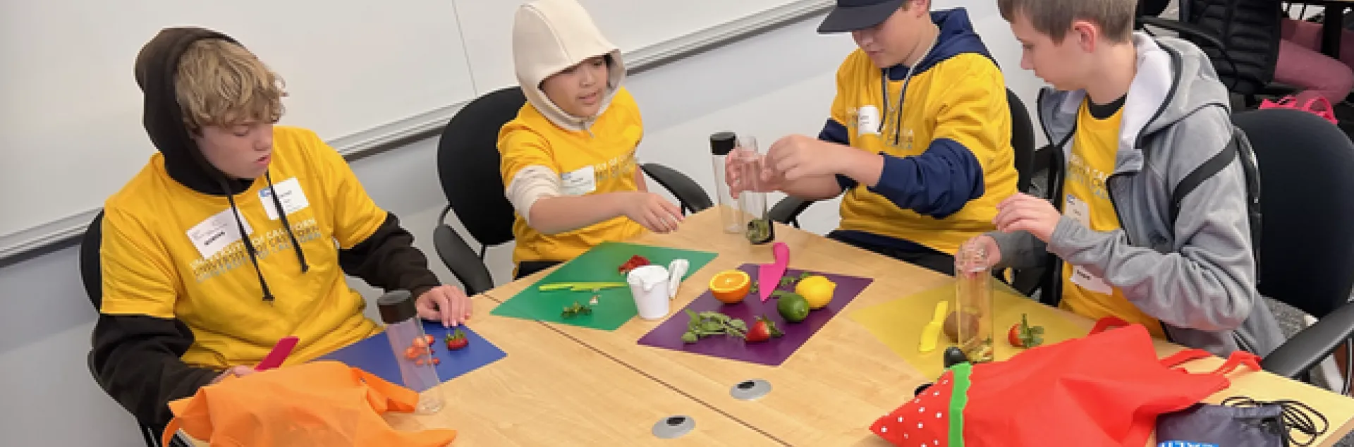 Four kids in yellow UC shirts slice citrus and berries to put in reusable bottles.