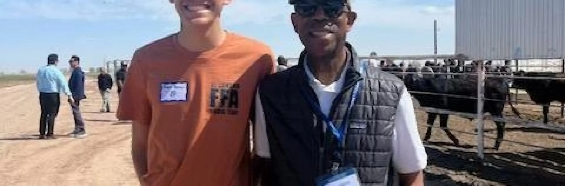 Young man stands next to President Drake with cows in the background.