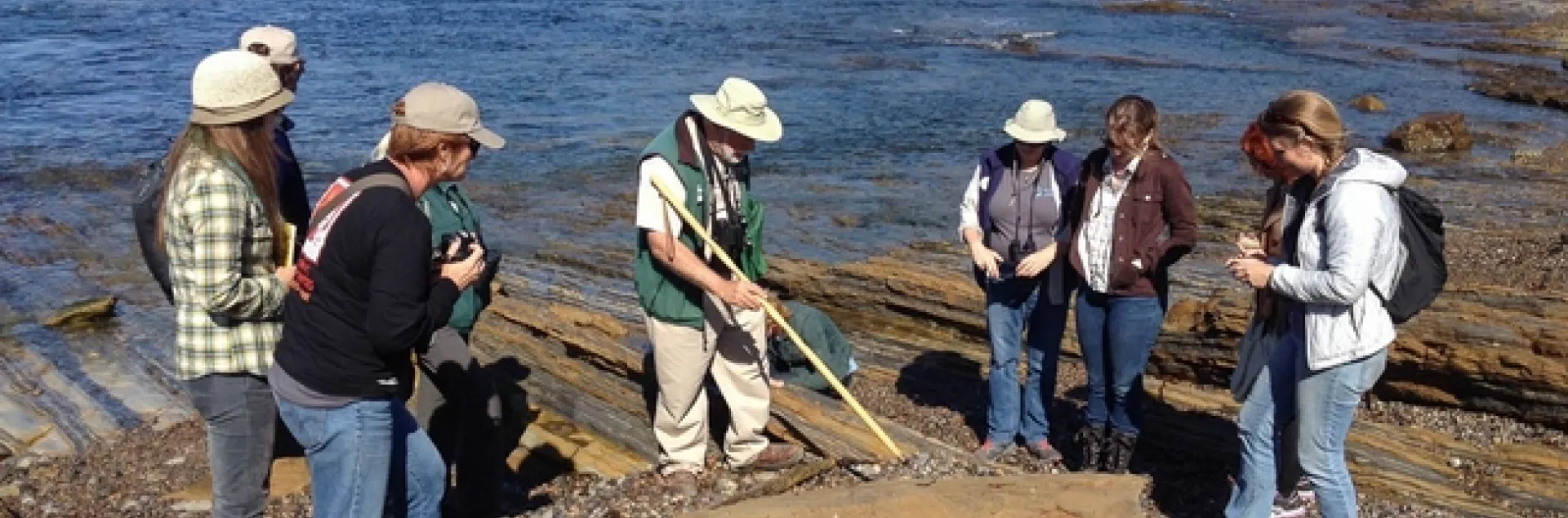 Eight people gather around Clifton as he points to fossils with a pole.