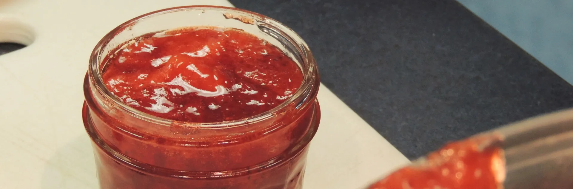 Half pint jar with the lid off showing glossy strawberry jam. 