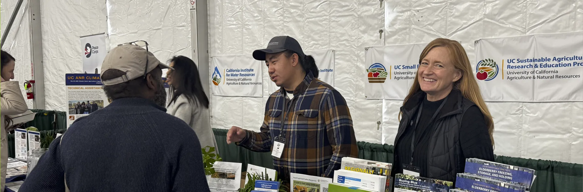 Two people and a participant at the UC ANR Organic Agriculture booth during Ecofarm 2026.