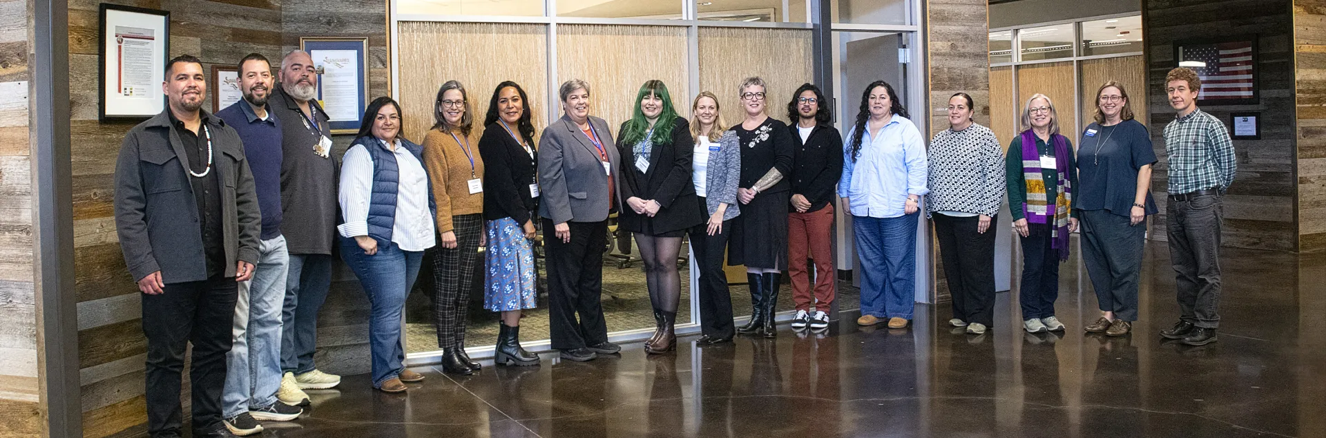 Sixteen people stand posing outside of the Coast Room