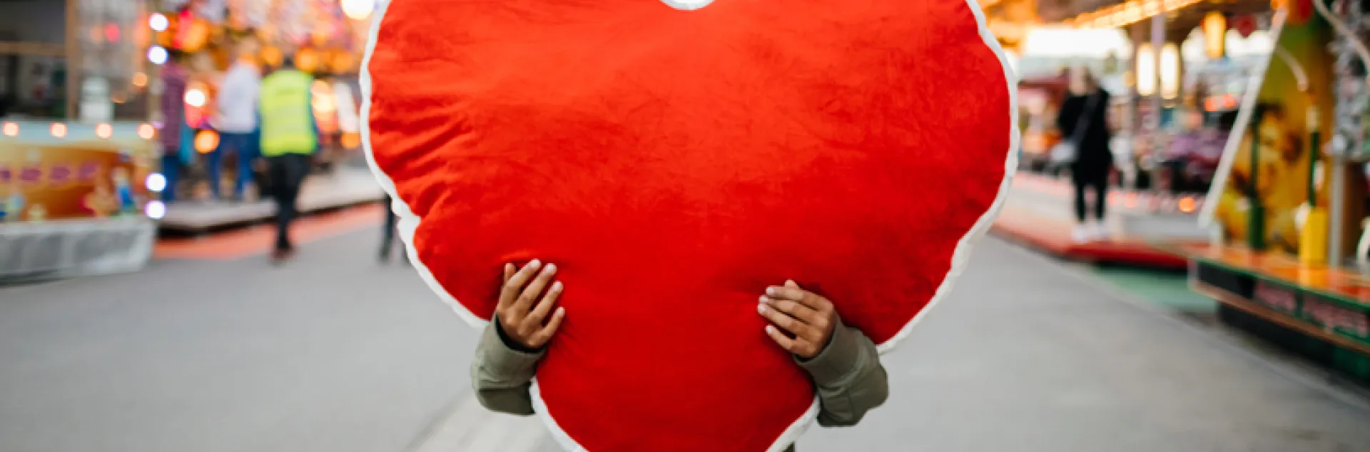 person holding a large stuffed heart covering their face on a busy street