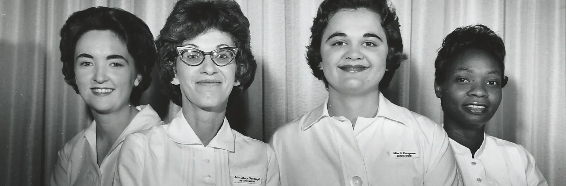 Three white women and one Black woman wearing white uniforms