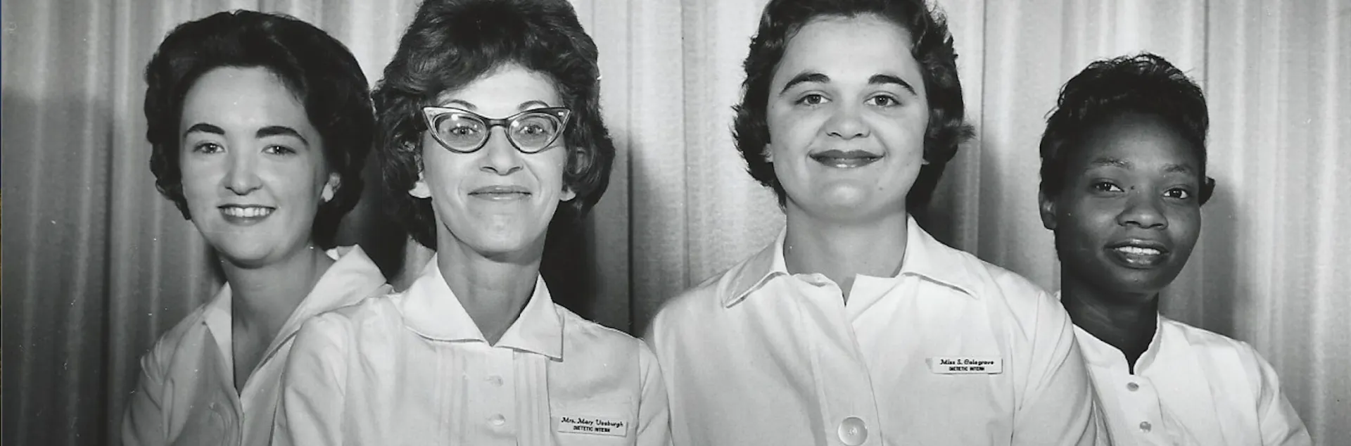 Three White women and one Black woman wearing white uniforms pose in a black and white photo