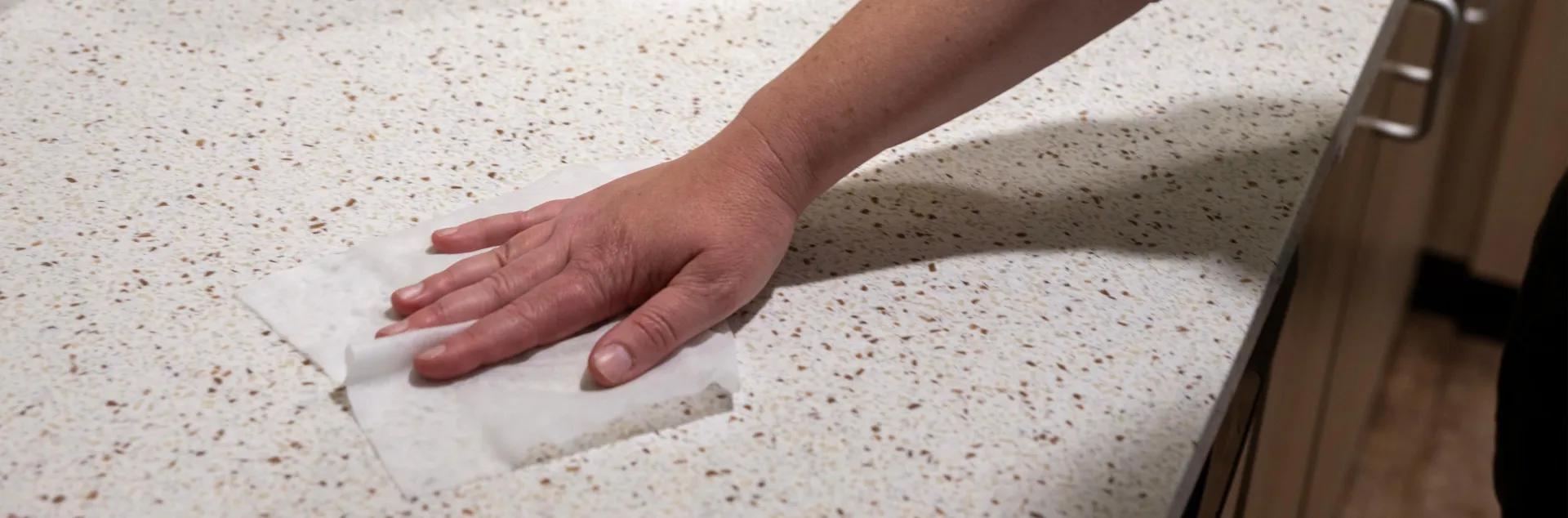 A person's arm wiping a white marble kitchen countertop with a white disinfectant wipe.