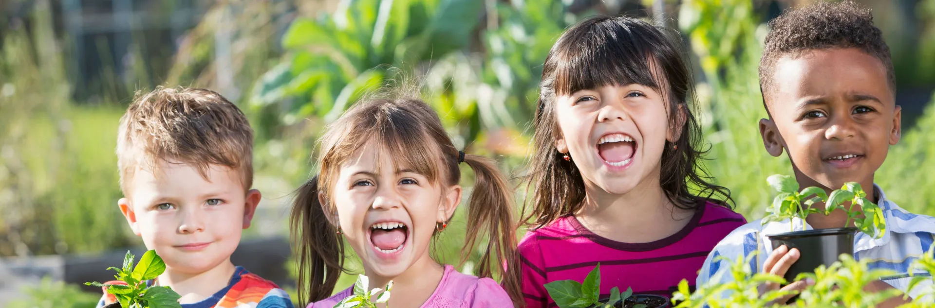 Four young children smile holding potted plants.