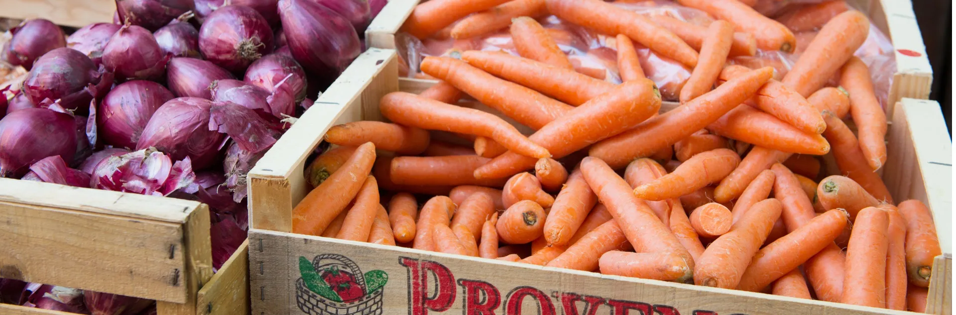 Purple onions and orange carrots in wooden crates