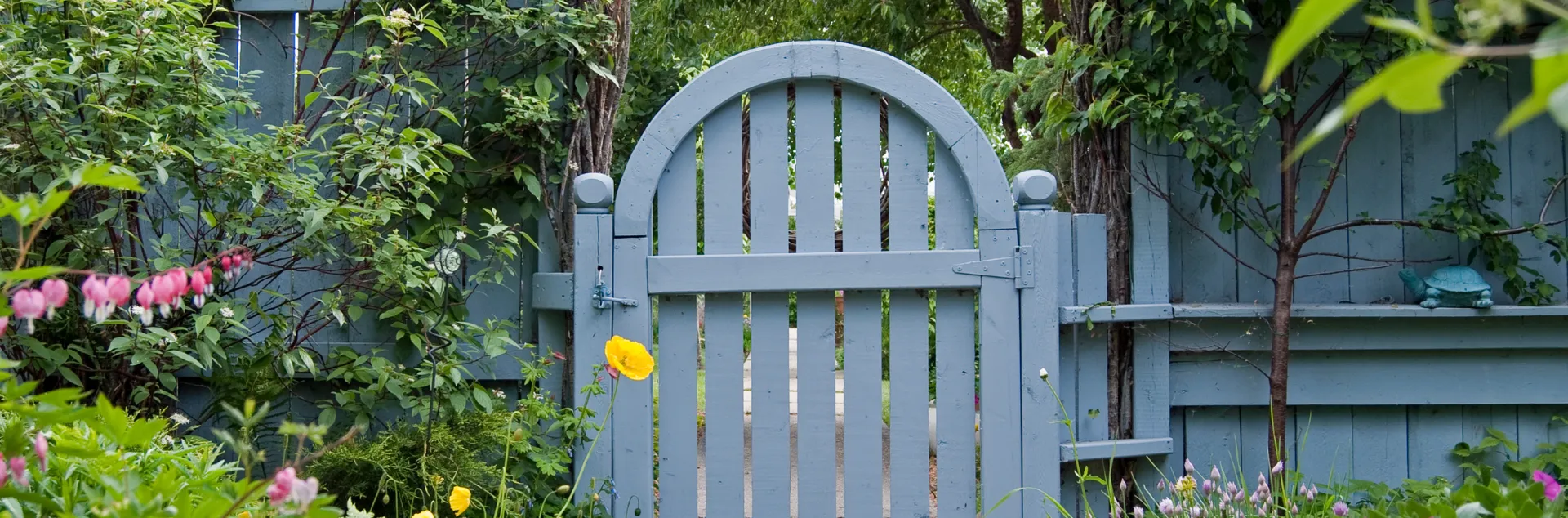 Gray arched garden gate and fence surrounded by plants