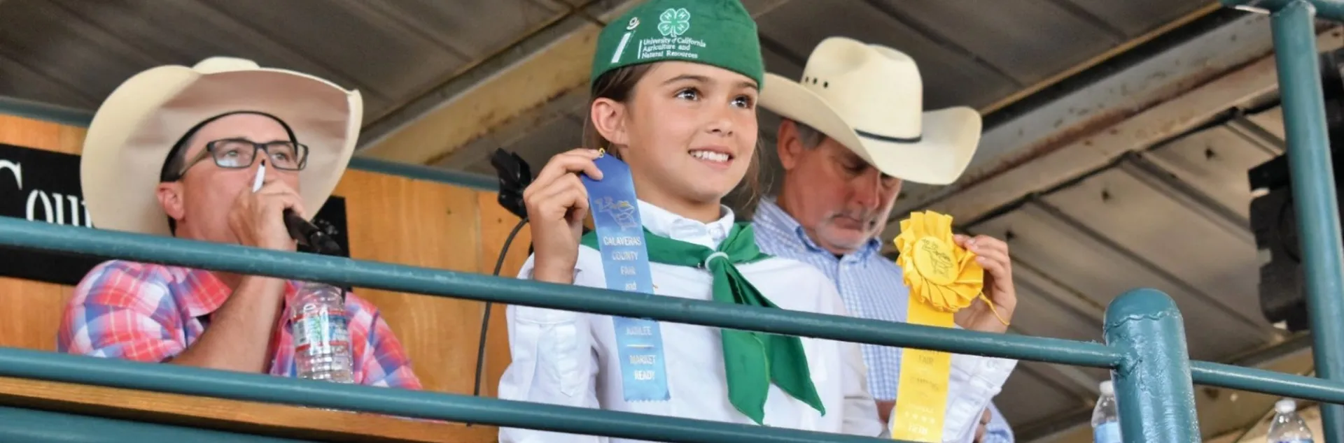 Girl in 4-H uniform holding blue and yellow ribbons at the fair