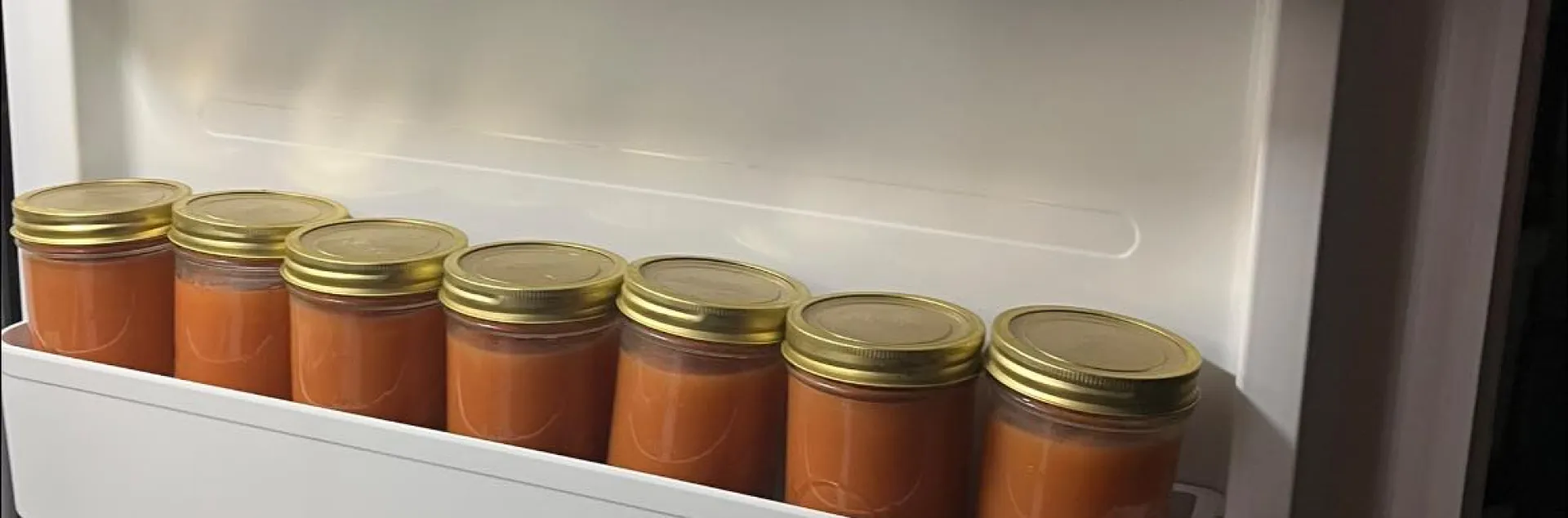 Inside of a freezer door, three rows of freezer jam in straight-sided glass jars with at least 1/2 inch of headspace