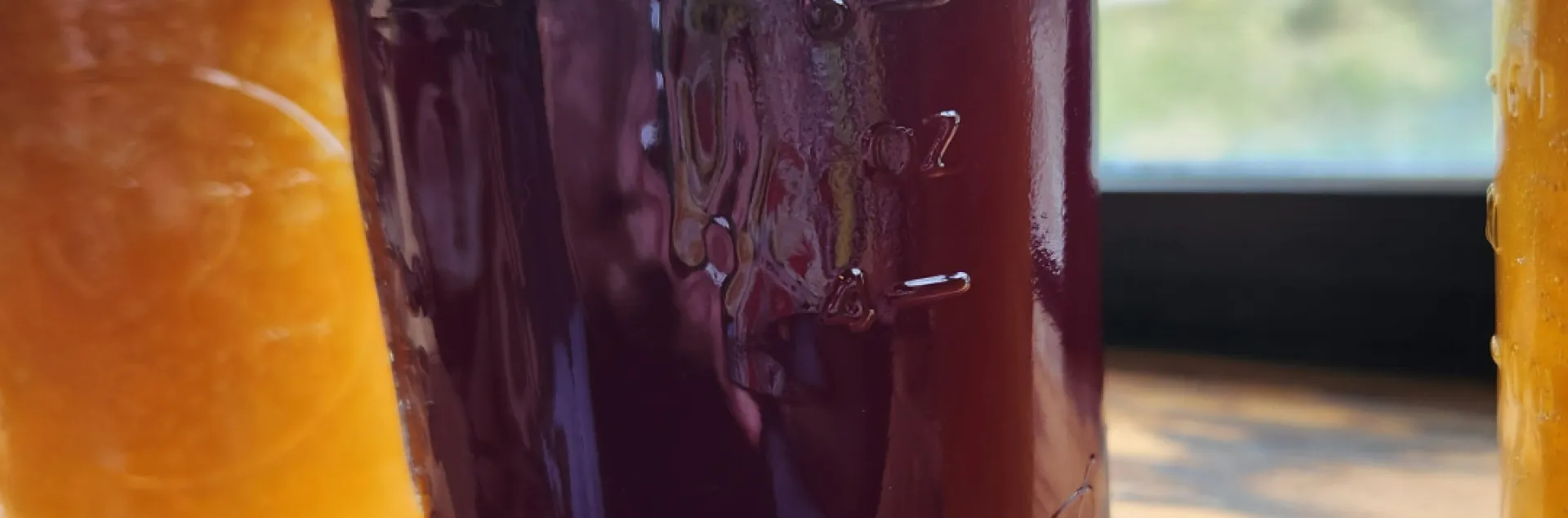 Backlit jars of red pomegranate jelly and orange peach jam on a wooden windowsill.