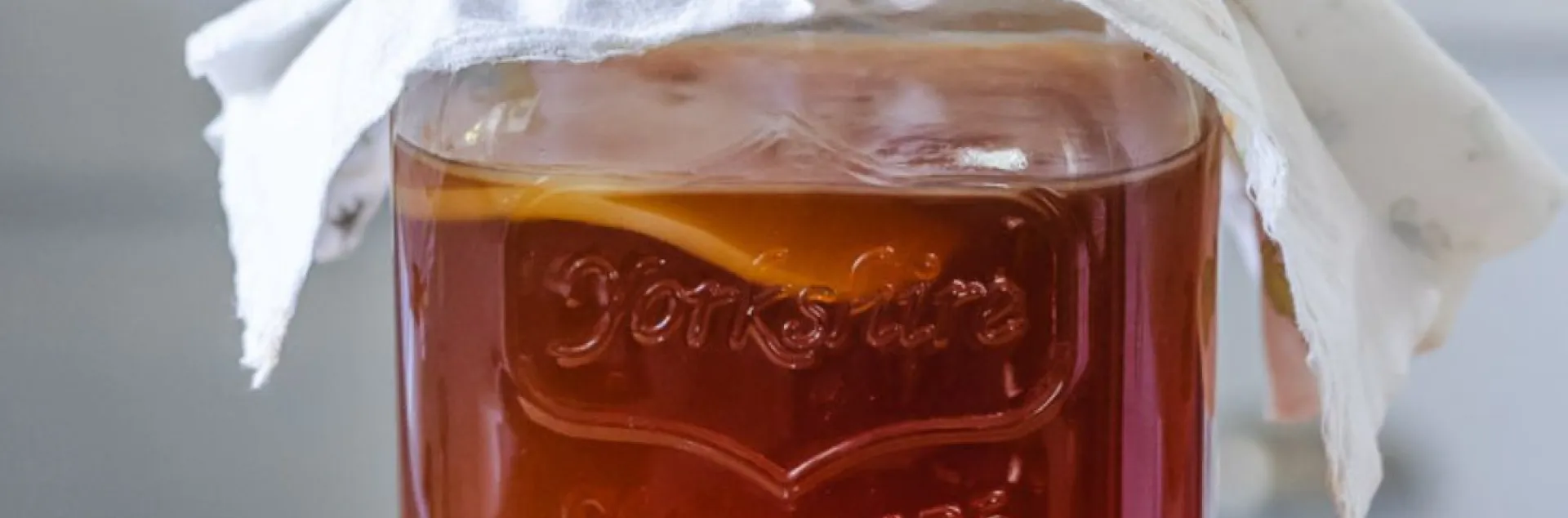 Large glass jar of kombucha with cloth cover