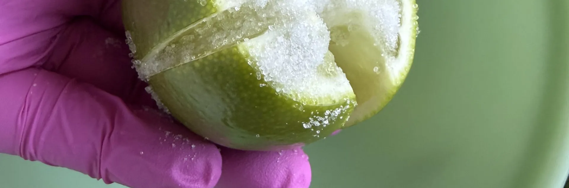  gloved hand holds a quartered lime covered in salt over a bowl