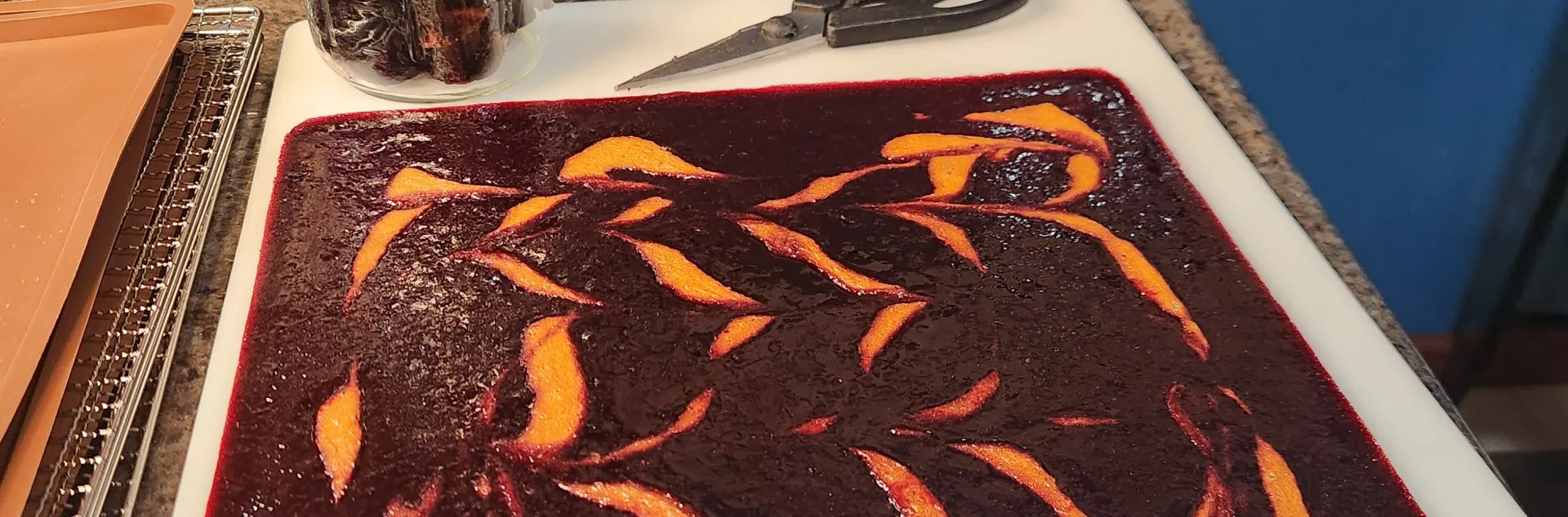 a rectangle of dehydrated berry and apricot puree on a cutting board next to a pair of scissors