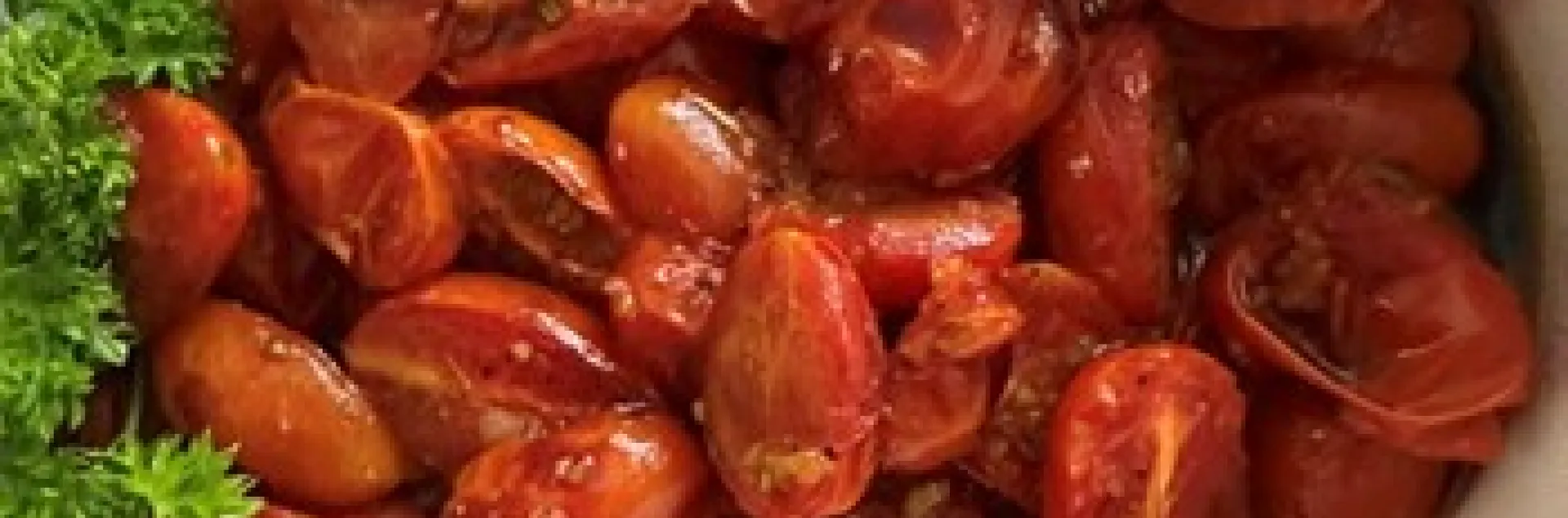 Roasted cherry tomatoes in a white bowl with a green garnish